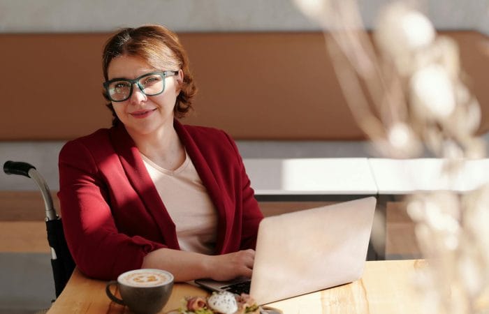 Smiling woman in red blazer using a laptop at a café table, enjoying her workday
