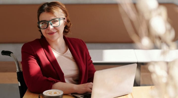 Smiling woman in red blazer using a laptop at a café table, enjoying her workday